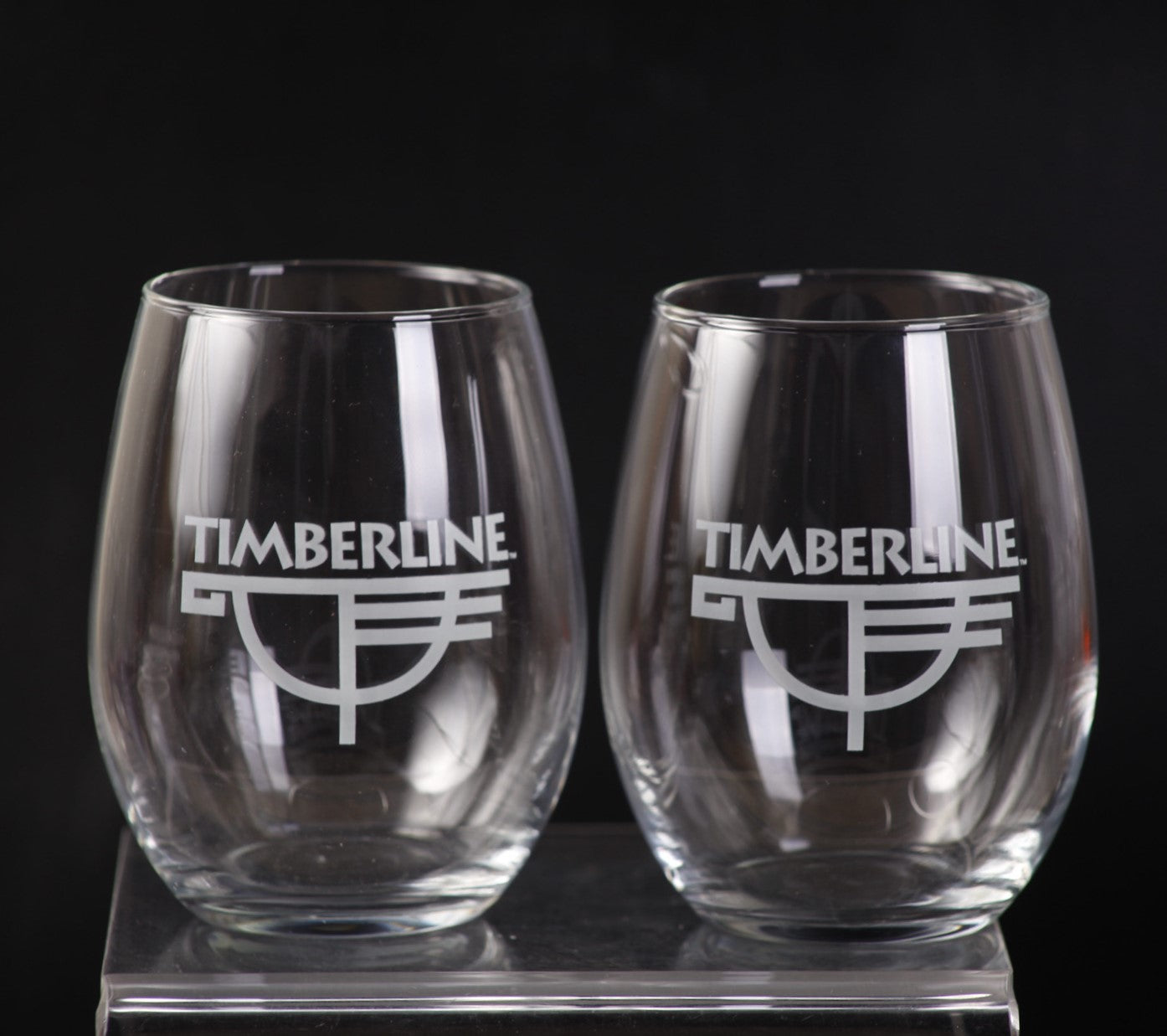 Two clear stemless wine glasses with 'Timberline' logo on a black background